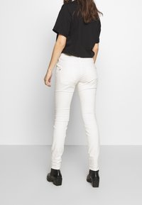 Pantalones vaqueros skinny blancos de mezclilla, con bolsillos traseros y diseño ajustado, combinados con una camiseta negra holgada y botas negras de tacón.