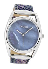 Montre argentée avec un cadran rond bleu irisé et des aiguilles argentées. Le bracelet présente un motif texturé violet et vert.