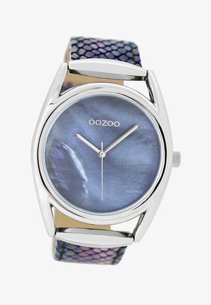Montre argentée avec un cadran rond bleu irisé et des aiguilles argentées. Le bracelet présente un motif texturé violet et vert.