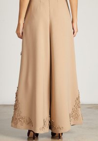 Pantalones de pierna ancha beige con bordado floral en el dobladillo, confeccionados en una tela suave. Cintura ajustada con un acabado limpio, diseño de largo completo.