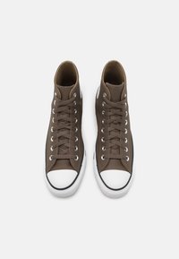Sneaker alte marroni con punta in gomma bianca, occhielli in metallo e tomaia testurizzata, dotate di lacci e una suola classica bianco e nera.