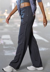 Dark gray athletic pants with a relaxed fit, featuring side buttons and an elastic waistband, paired with white sneakers.