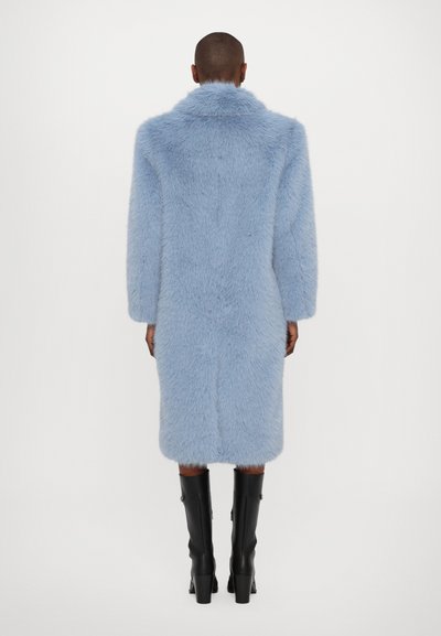Abrigo de pelaje sintético en azul claro con un cuello alto, de longitud hasta la rodilla, con mangas largas y una forma recta. Combinado con botas negras hasta la rodilla.