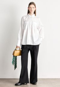 Fehér gombos ing két mellzsebbel, fekete, bőszárú nadrággal párosítva. Kiegészítők: egy kis sárga kézitáska és egy zöld mintás kendő.