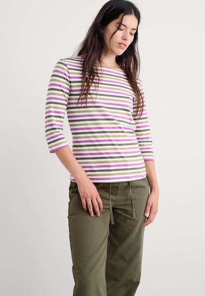 Gestreiftes Langarmshirt mit lila, olivgrünen und weißen Streifen, einem runden Ausschnitt und dreiviertellangen Ärmeln. Kombiniert mit olivgrünen Hosen.