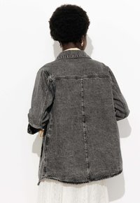 Veste en denim grise surdimensionnée avec une texture décolorée, des coutures visibles et un col classique. Le dos présente un ourlet arrondi.