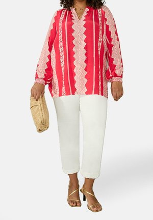 Rot-weiß gestreifte Bluse mit langen Ärmeln und V-Ausschnitt; kombiniert mit weißen cropped Hosen und goldenen Riemchensandalen. Hält eine beige Clutch.