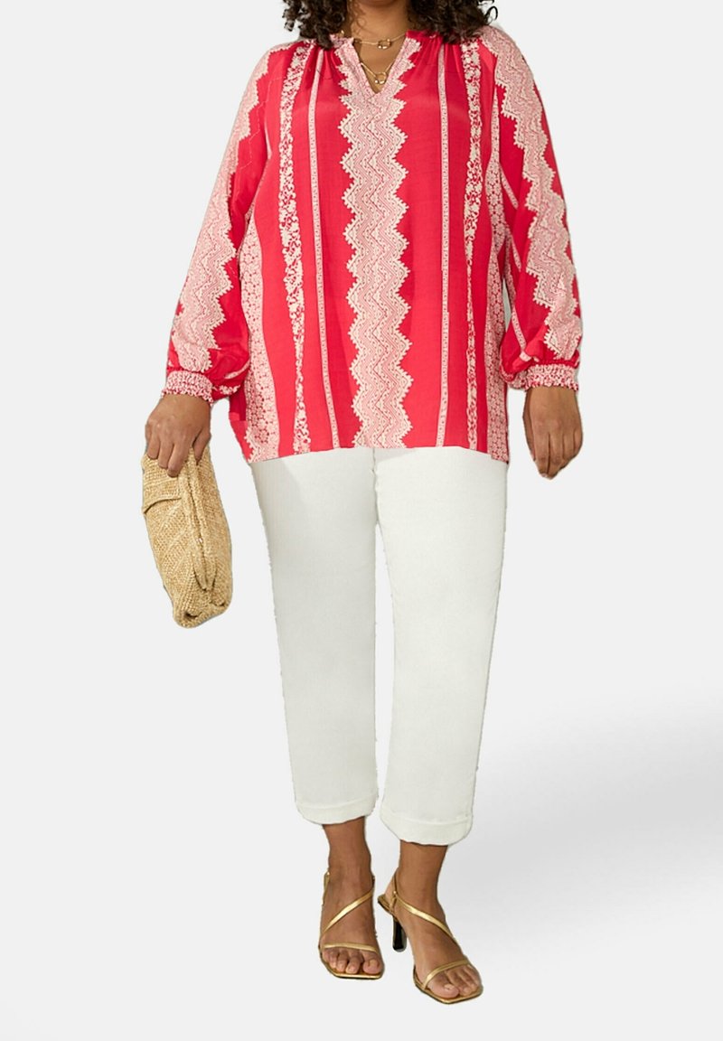 Rot-weiß gestreifte Bluse mit langen Ärmeln und V-Ausschnitt; kombiniert mit weißen cropped Hosen und goldenen Riemchensandalen. Hält eine beige Clutch.