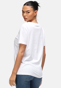 Bílá bavlněná tričko s krátkým rukávem, kulatým výstřihem a volným střihem, v kombinaci s modrými džíny. Minimalistický design.