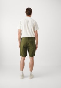 Camicetta bianca a maniche corte in tessuto testurizzato con colletto aperto, abbinata a pantaloncini verde oliva arrotolati e sneakers bianche.