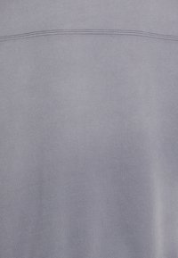 Pehmeä harmaa kangas, jossa vaakasuora ommeltu sauma lähellä yläreunaa, esittäen sileää koostumusta ja hienovaraisia värivariaatioita.