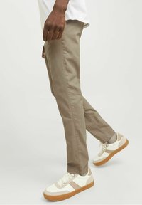 Béžové bavlněné kalhoty s úzkým střihem a bočními kapsami, doplněné bílými teniskami s béžovými detaily a gumovou podrážkou. Ležérní outfit.