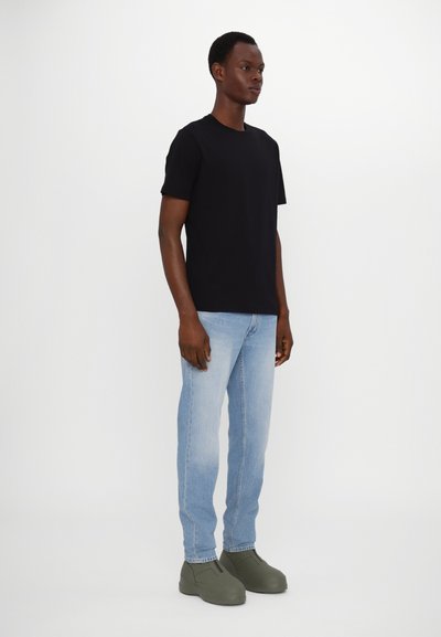 T-shirt en coton noir, jeans en denim bleu clair et sabots vert foncé. Design simple avec des manches courtes et un fit droit pour les jeans.