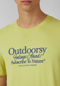 Limoengroene katoen t-shirt met korte mouwen, met blauwe bedrukte tekst die luidt: "Buitengevoelens Vooruit! Abonneer je op de Natuur®."