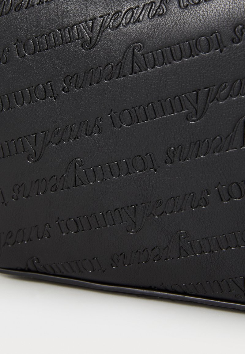 Funda de cuero negro con el nombre de la marca "tommyjeans" en relieve y en un patrón repetido. Textura suave, forma rectangular, diseño minimalista.