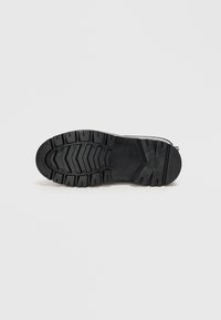 Semelle de chaussure en caoutchouc noir avec un motif de semelle robuste, comprenant des rainures et des arêtes pour une traction, et présentant une zone de talon lisse.