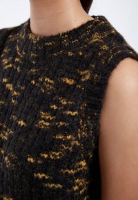 Stickad ärmlös tröja i svart med gyllene fläckar. Har en hög, ribbad krage och en texturerad tyg med ett mönstrat design.