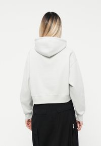 Felpa grigia tagliata con un ampio cappuccio, maniche raglan e polsini a coste. Abbinata a una gonna nera con tasche.