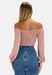 Top rosa chiaro con spalle scoperte, dotato di un corpino arricciato e maniche lunghe, abbinato a una gonna di jeans a vita alta con zip sul retro.