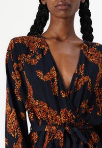 Mornarško oblačilo z oranžnim abstraktnim vzorcem, V-izrez, dolgi rokavi, zoženo v pasu z vezalko iz tkanine, teksturirana tkanina.