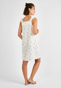 Nottura bianca floreale con spalline arricciate, design al ginocchio e un tessuto morbido e texturizzato con piccoli fiori rosa e accenti verdi.