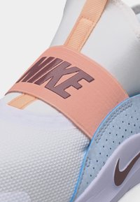 Λευκό και ανοιχτό μπλε αθλητικό παπούτσι Nike με υφασμένο επάνω μέρος, ροδακινί λουράκι στη μέση του ποδιού με μεγάλο λογότυπο Nike σε καφέ χρώμα.