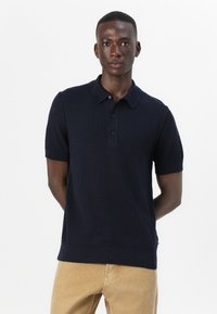 Polo a maniche corte blu navy in tessuto texturizzato, con patta a due bottoni e colletto classico, abbinato a pantaloni beige.
