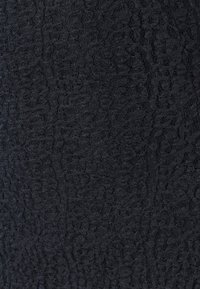 Svart texturerat tyg med ett subtilt, upphöjt mönster. Materialet verkar mjukt med en lätt genomskinlig kvalitet, lämpligt för olika designer.