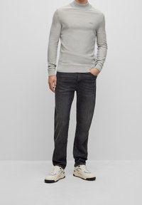 Ljusgrå, ribbstickad polotröja med smal passform; kombinerad med mörka jeans och vita sneakers med svarta detaljer.