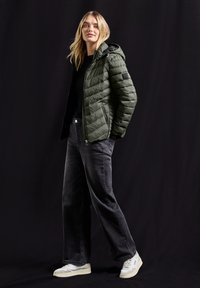 Grön puffjacka med kviltad textur, med dragkedjefickor och huva, kombinerad med svarta vida jeans och vita sneakers.