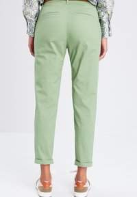 Pantalons en coton vert clair avec des poignets retroussés et des poches arrière, associés à des baskets blanches avec des accents beige.