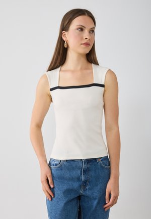 Witte geribde tanktop met vierkante halslijn en zwarte accentstreep over de borst. Gecombineerd met blauwe high-waisted denim jeans.