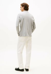 Camicia a maniche lunghe grigia chiara, in misto cotone, con un colletto semplice. Abbinata a jeans bianchi e mocassini neri, vista da dietro.