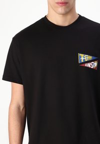 Black cotton t-shirt featuring a colorful, embroidered logo with fragmented text and triangular shapes on the chest. Short sleeves.