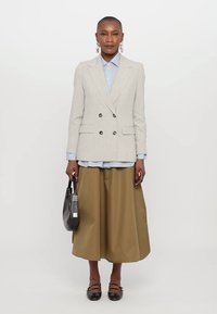 Lys grå dobbeltspent blazer over en blåstripet skjorte, kombinert med en khaki midi-skjørt. Modellen holder en svart veske, med mørke sko.
