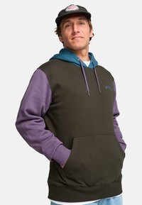 Sudadera con capucha que presenta un cuerpo de color verde oscuro, mangas moradas y capucha azul. Mezcla de algodón con un bolsillo delantero y cordones ajustables.