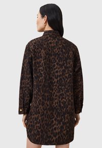 Abito camicia in denim con stampa leopardata marrone e nera, dotato di colletto, maniche lunghe e una vestibilità comoda. Dettagli con bottoni dorati ai polsini.