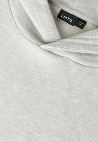 Sudadera con capucha gris claro con una textura suave, cuello ancho y una etiqueta que dice "LMTD" con detalles de talla visibles.