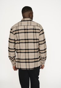 Beige kariertes Hemd mit schwarzen und braunen Streifen, langen Ärmeln, Knopfmanschetten und einer Rückenpasse. Hergestellt aus weichem, strukturiertem Stoff.