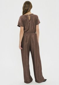 Bronz színű, fémes overál, széles lábakkal és rövid ujjakkal. Derékpánttal és egy kis kulcslyuk részlettel rendelkezik a hát nyakvonalán.