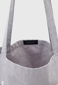 Borsa a tracolla grigia in tela con manici lunghi, caratterizzata da una texture liscia e un'etichetta interna che reca la scritta "ALLSAINTS". Design semplice e funzionale.