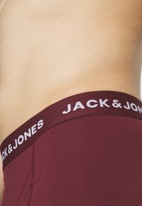 Bordeauxfarbene Boxershorts mit breitem elastischen Bund, der den weißen Text "JACK & JONES" zeigt. Glattes Material und figurbetontes Design.