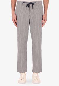 Pantaloni a righe grige con vita regolabile, dal texture morbido e gambe affusolate, abbinati a sneakers bianche.