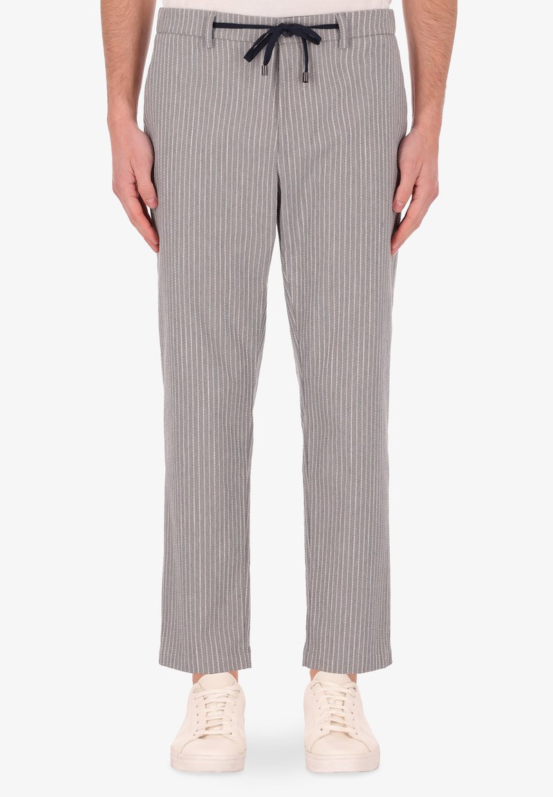 Pantaloni a righe grige con vita regolabile, dal texture morbido e gambe affusolate, abbinati a sneakers bianche.