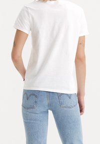 Camiseta de algodón blanca con cuello redondo, mangas cortas y un ajuste holgado, combinada con jeans de mezclilla azul claro con bolsillos traseros y detalles de costura.