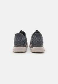 Dark gray slip-on shoes with a textured upper, flexible sole, and contrasting beige rubber outsole. Features pull tabs for easy wear.