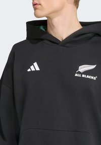 Sort hoodie lavet af en bomuldsblanding. Har en frontkangaroo-lomme, stort hvidt logo og grøn inderside i hætten.