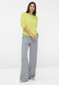 Hellgrüner gestrickter Pullover mit aufgeschlagenen Bündchen, kombiniert mit grauen, gestreiften, weiten Hosen. Elegante silberne Schuhe runden das Outfit ab.