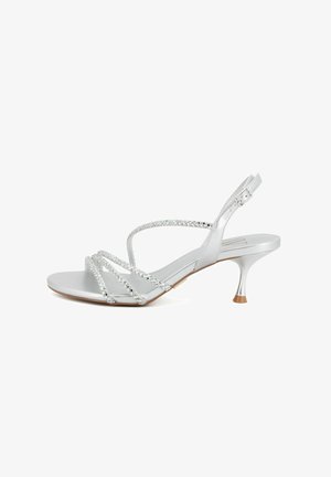 Sandalo argento con tre sottili cinturini intrecciati davanti, cinturino alla caviglia con fibbia e tacco basso curvo con punta color cuoio.