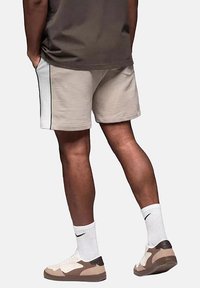 Shorts en coton beige avec des rayures latérales blanches, associés à des chaussettes blanches et des chaussures multicolores. Le design est décontracté et de longueur mi-longue.